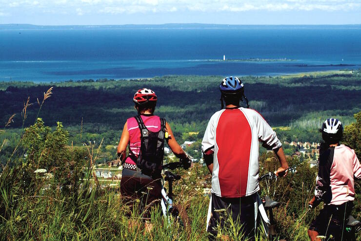 Three cyclists standing with bikes on top of Blue Mountain looking a view of lake