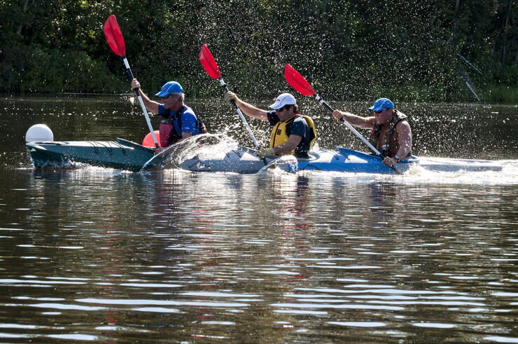 Three men in a kayak paddling hard. 