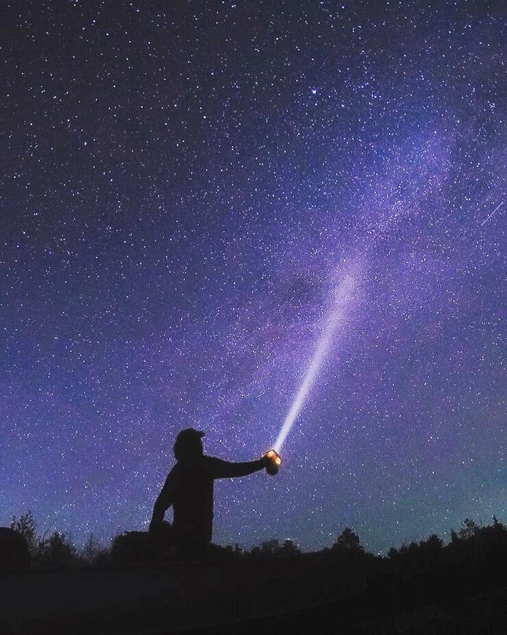 Man pointing a flashlight into the dark starry night sky. 