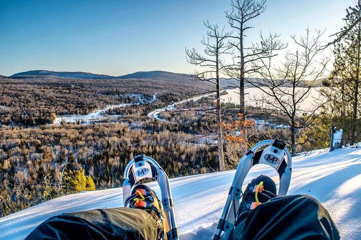Looking down at a person's boots with snowshoes from a high vista.