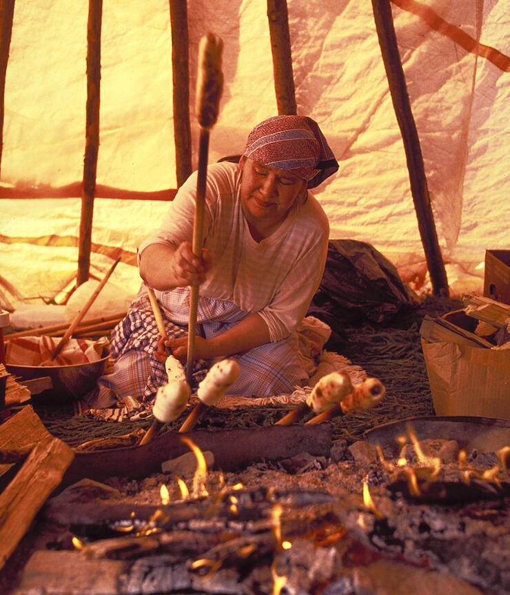 Cree woman making bannock over a fire