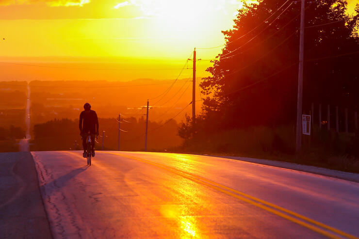 Cyclist riding into sunset on a country road.