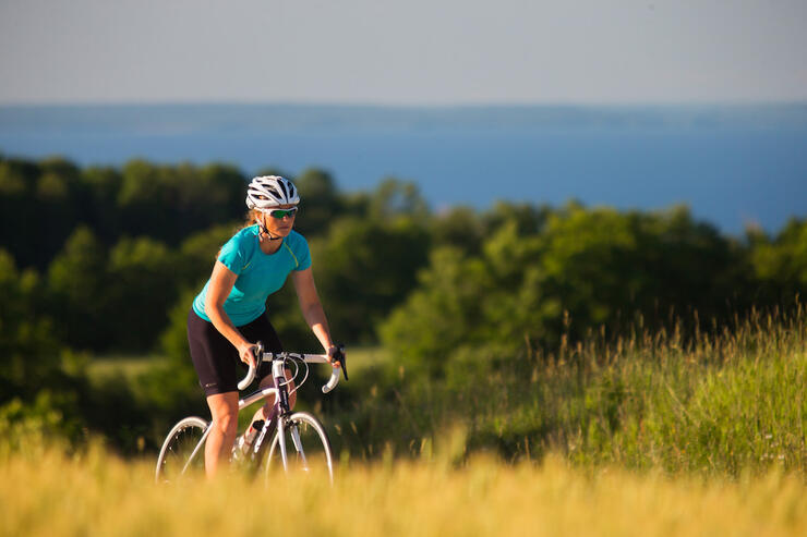 Woman cycling up a hill in summer with view of Georgian Bay.