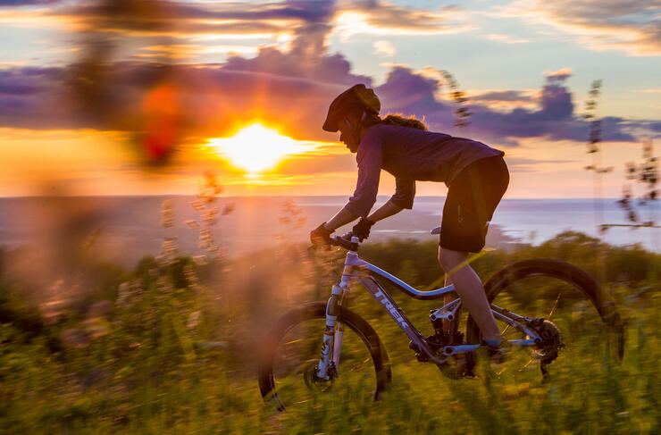 Mountain biker riding on trail with Georgian Bay and sunset in background
