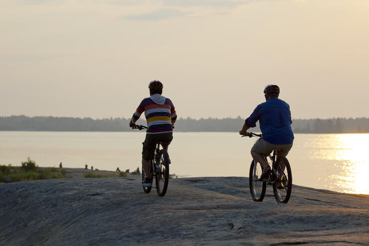 Two people riding bikes across flat rock near a lake