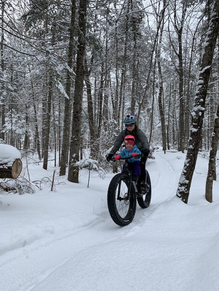 Mother and daughter ride a fat bike along a snowy forest trail in winter