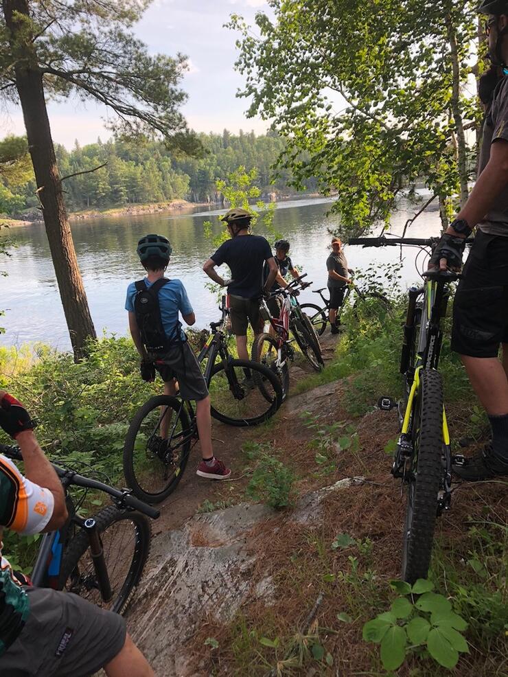 A group of adults and children pause by the water while mountain biking
