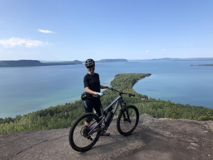 Person poses with bike at a lookout point over the water