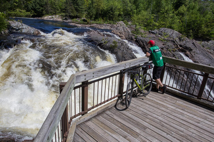 a cyclist stops on a wooden stairacase and looks at a waterfall in Chutes Provincial Park