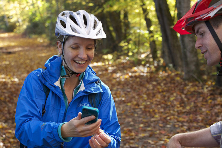 Woman and man look at an app on her cell phone while cycling a forest trail