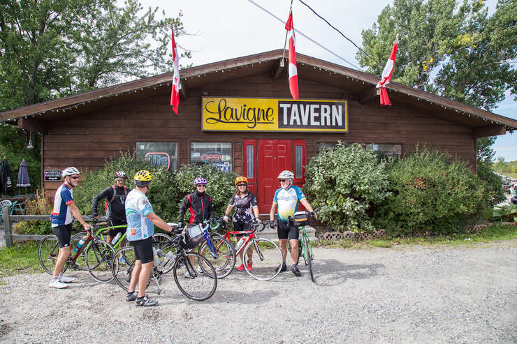 A group of cyclists stand in front of the Lavigne Tavern after a long bike ride