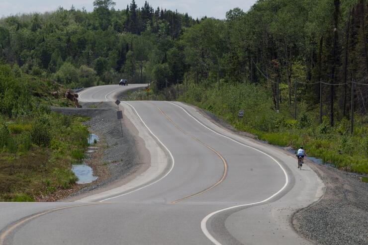 cyclist rides along the roadside through wooded hills