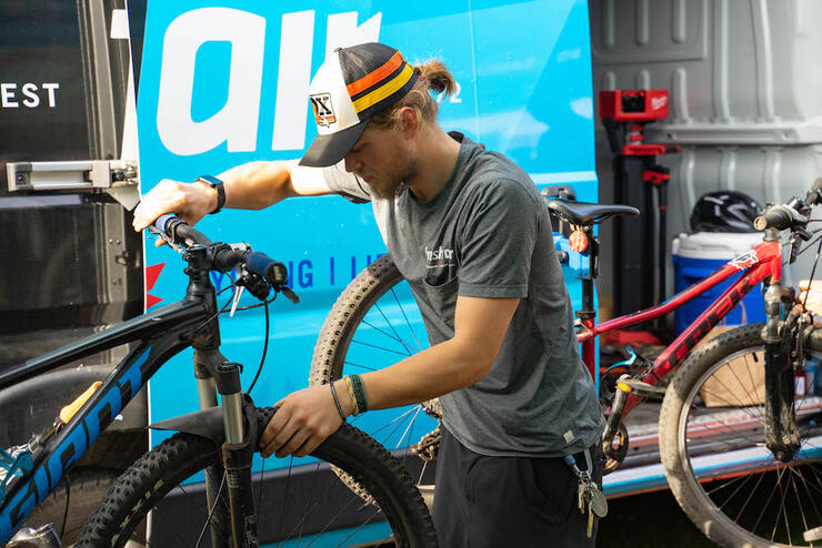 a bike mechanic tunes up a bicycle in front of an open tow trailer