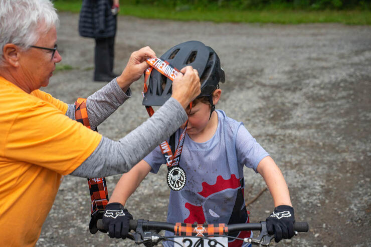 older woman puts a medal over the head of a helmeted child after a bike race
