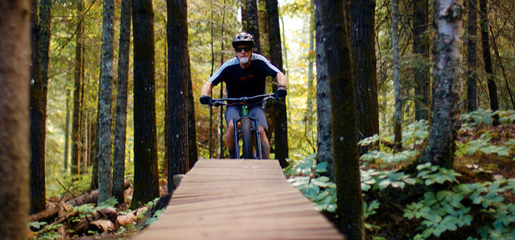 man riding bike approaches boardwalk feature on forested Shuniah Mines trail