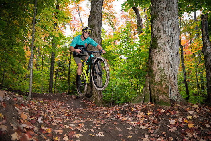 man jumps his bike while riding a forested trail at the Algoma Highlands Conservancy