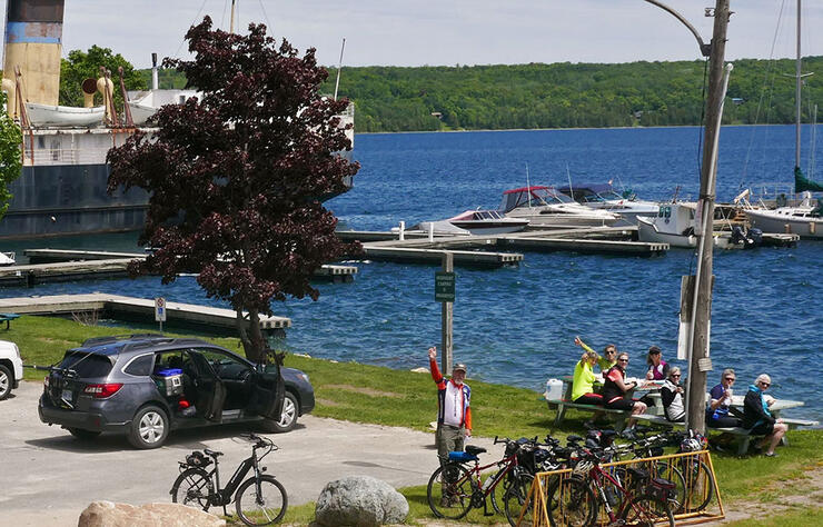 a group of touring cyclists stop for lunch at waterfront picnic tables near a marina