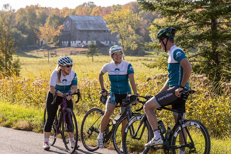 three cyclists on a guided tour stop for a break in front of picturesque barn in fall