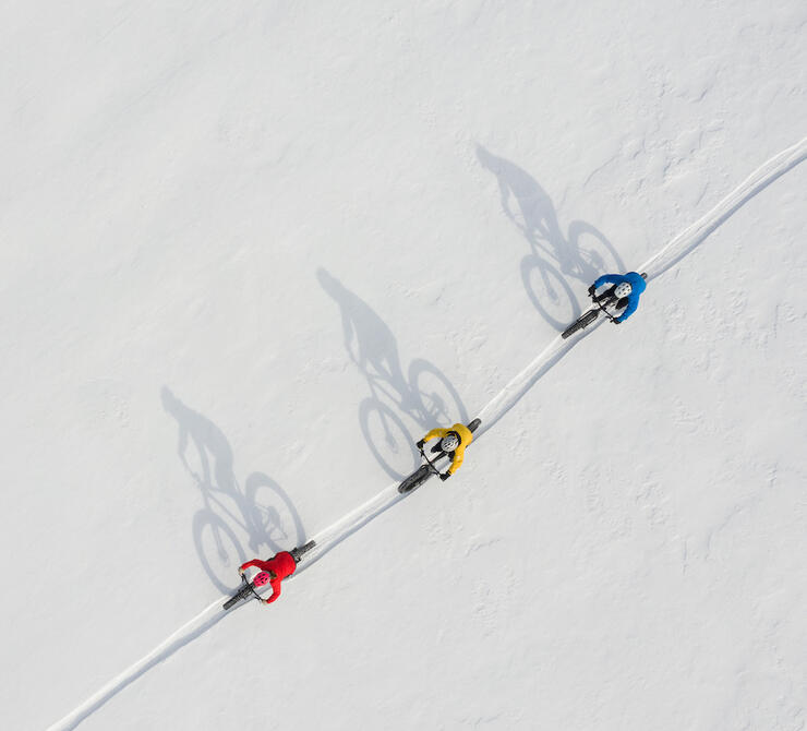 Aerial view of three fat bikers riding winter trail 