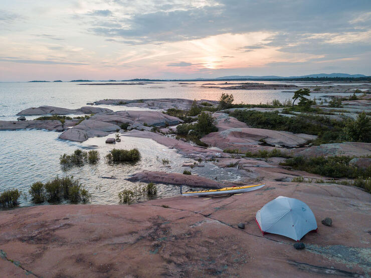 Tent and kayak on rocky shore.