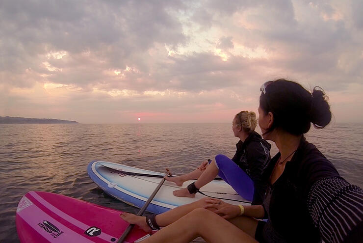 two women sit on paddleboards and watch the sunrise