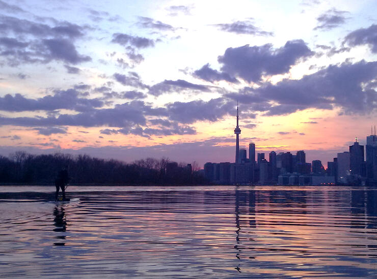 person paddles a SUP at dusk in front of the Toronto skyline