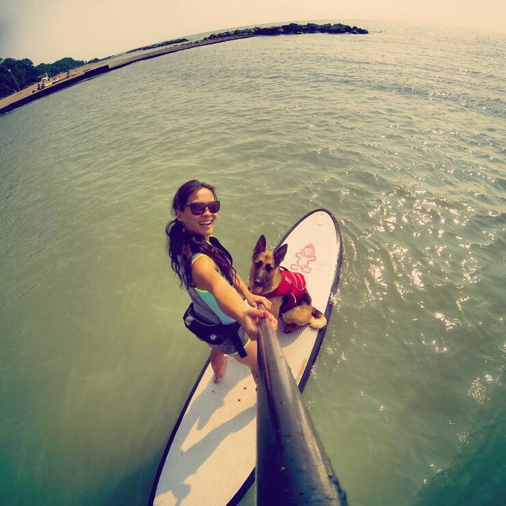 woman uses selfie stick to take photo on SUP with her german shepherd