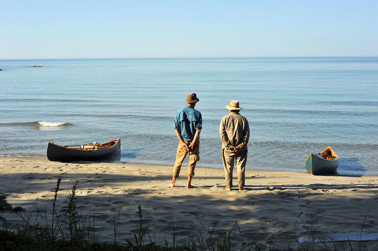 Two people stand on beach with canoe nearby