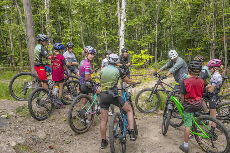 Emily and a group of young cyclists talk in a group on their bikes in the forest.