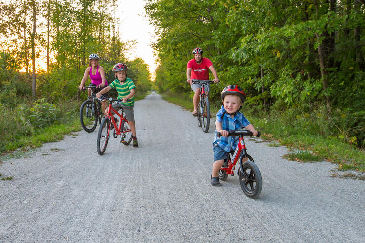 Mother, father and two young children on bicycles on rail trail. 
