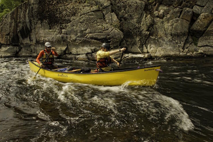 Two people in a yellow canoe paddling in rapids. 