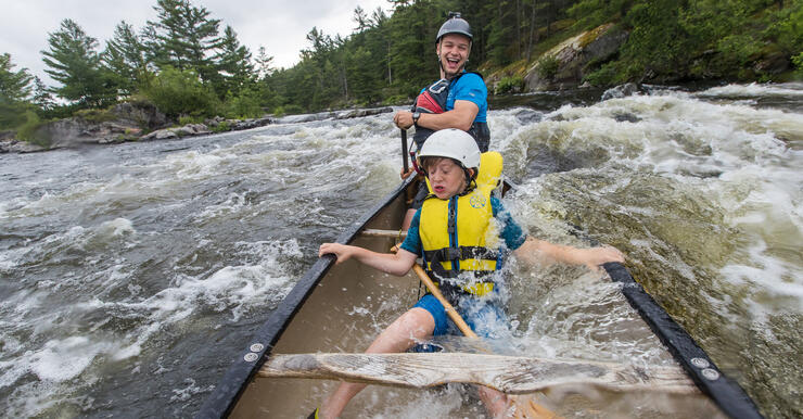 Child in mid-section of canoe with laughing guide in stern of canoe in whitewater rapids.