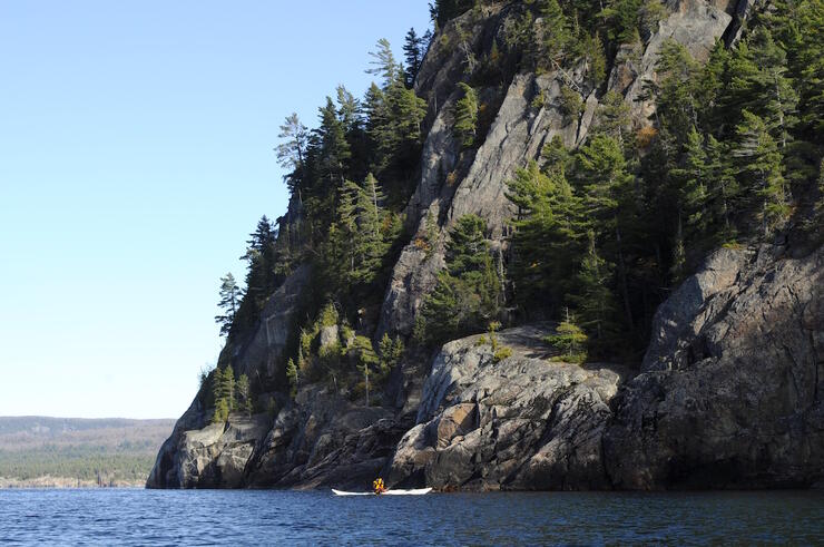 Kayaking paddling beside high rocky cliffs.
