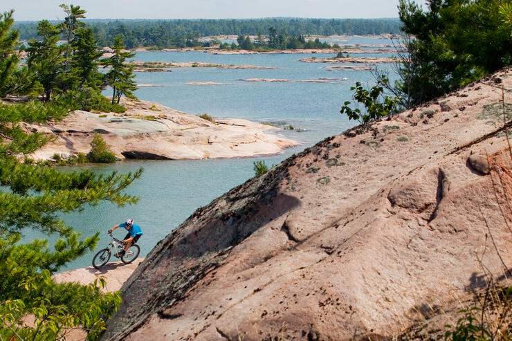 Mountain biker riding on pink granite rock along edge of Georgian Bay