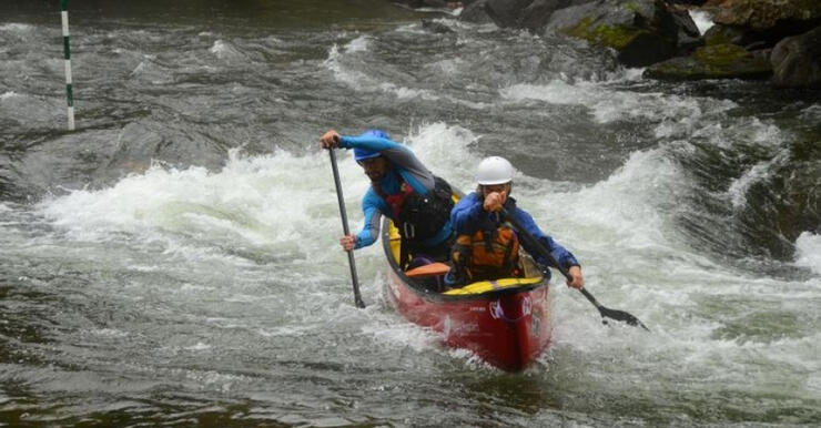 Two people with helmets and lifejackets in a red canoe paddling in whitewater rapids on Gull River.