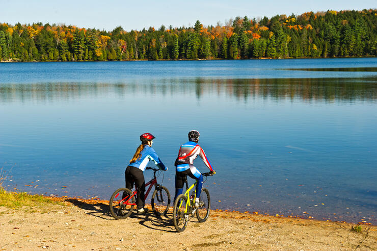 Two cyclists looking across a small lake at colourful forest. 