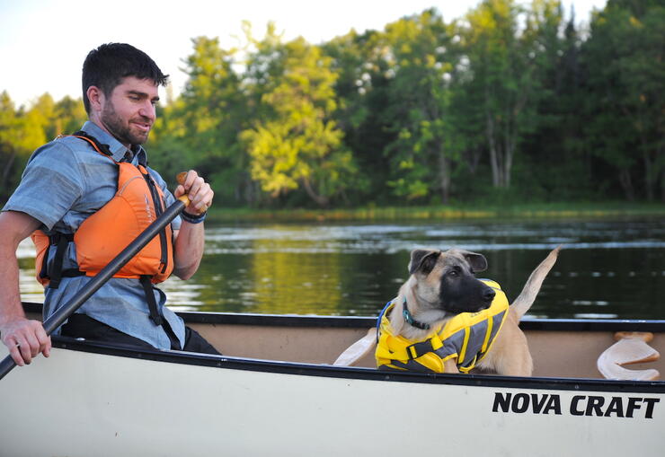 Man paddling a small dog in a canoe.