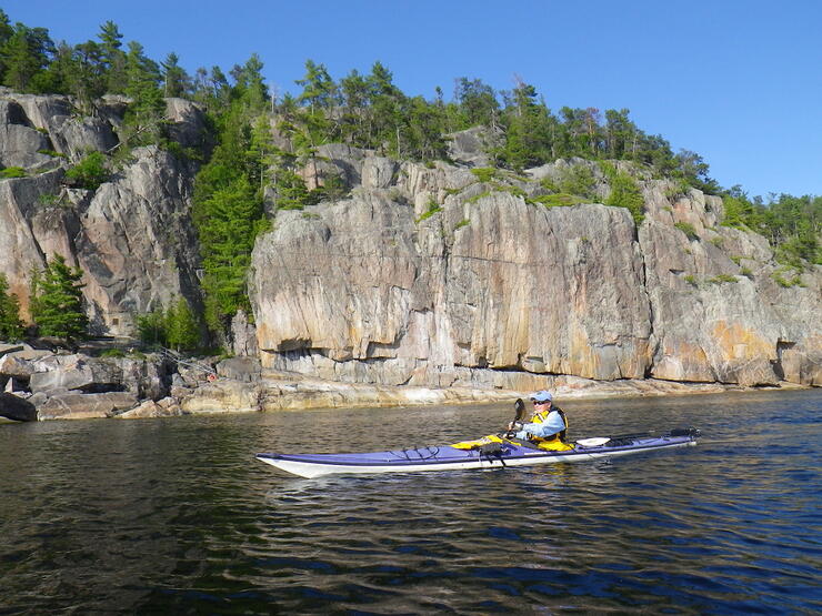 Sea kayaker paddling beside rock cliffs