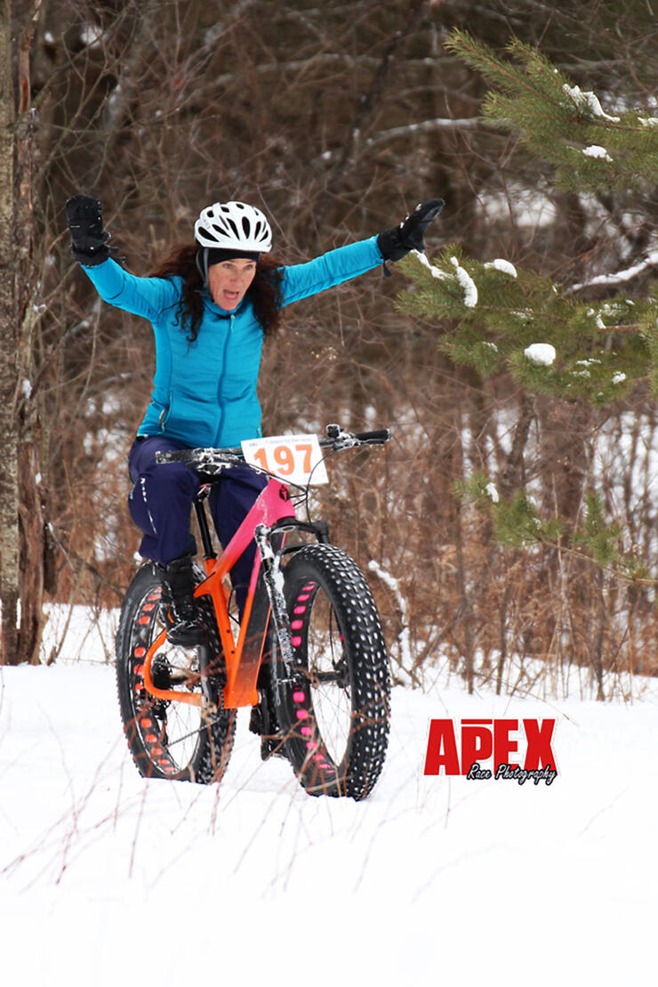 woman raises her hands in excitement while fat biking in winter