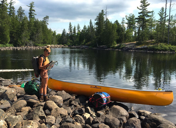Woman standing beside a yellow canoe on a rocky shoreline