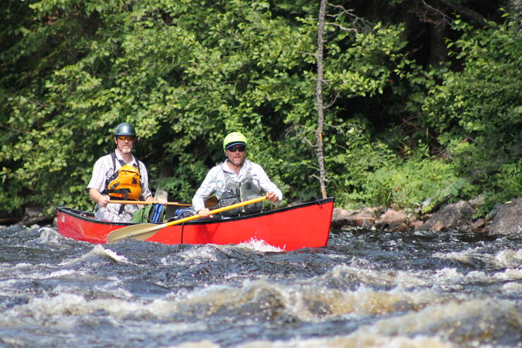 Two men in red canoe paddling on a whitewater river