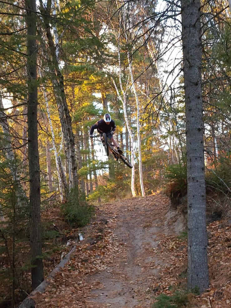 man jumps mountain bike over a hill in the forest near Kenora