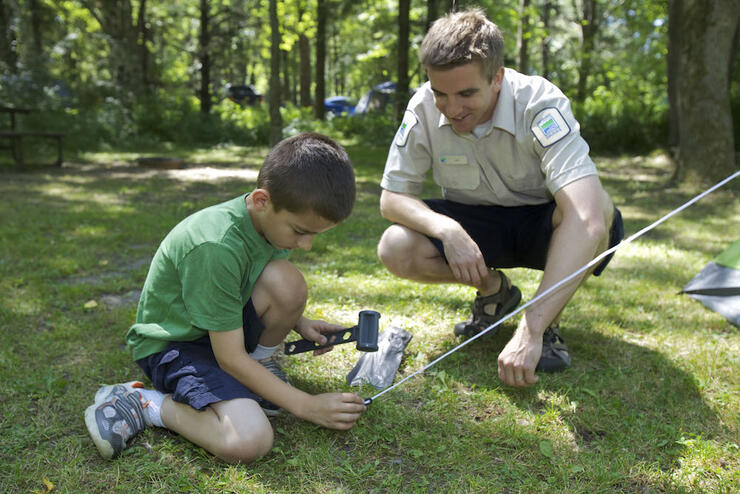 Ontario Parks staff helping a child with a tent peg while setting up a tent for camping in Ontario.