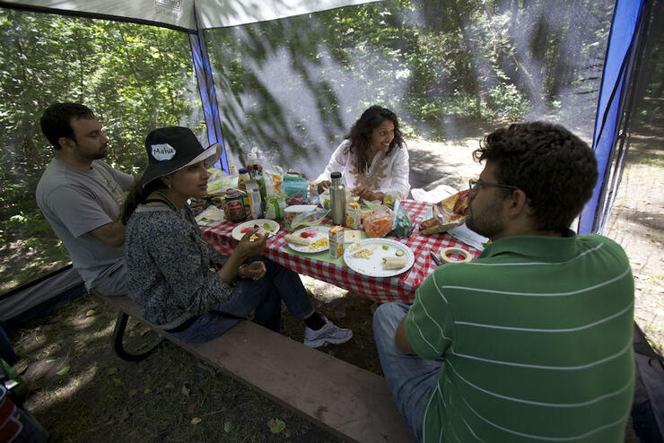 Group of people sitting at a picnic table with screened tent over it. 