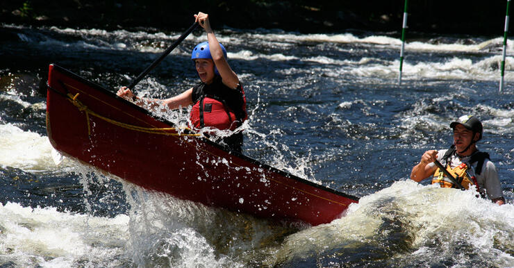 A red canoe with two people paddling in whitewater rapids. 