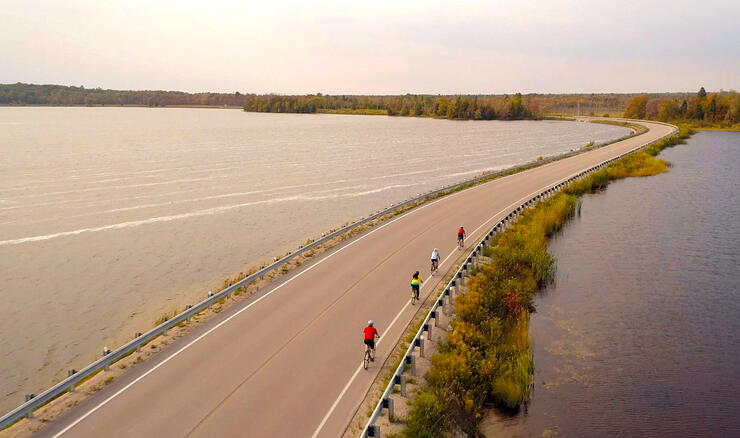 Group of cyclists riding on paved shoulder over causeway. 