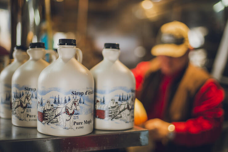 Jugs of maple syrup with man in background.