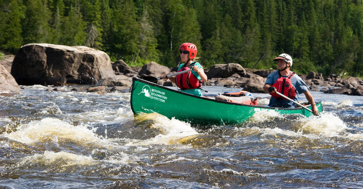 Two people paddling in green canoe in whitewater rapids