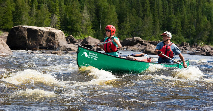 Two people paddling in green canoe in whitewater rapids 