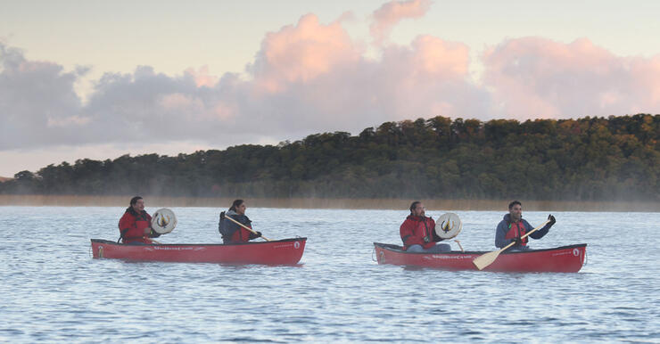 two red canoes on lake surrounded by light mist, Indigenous guides with drums in stern